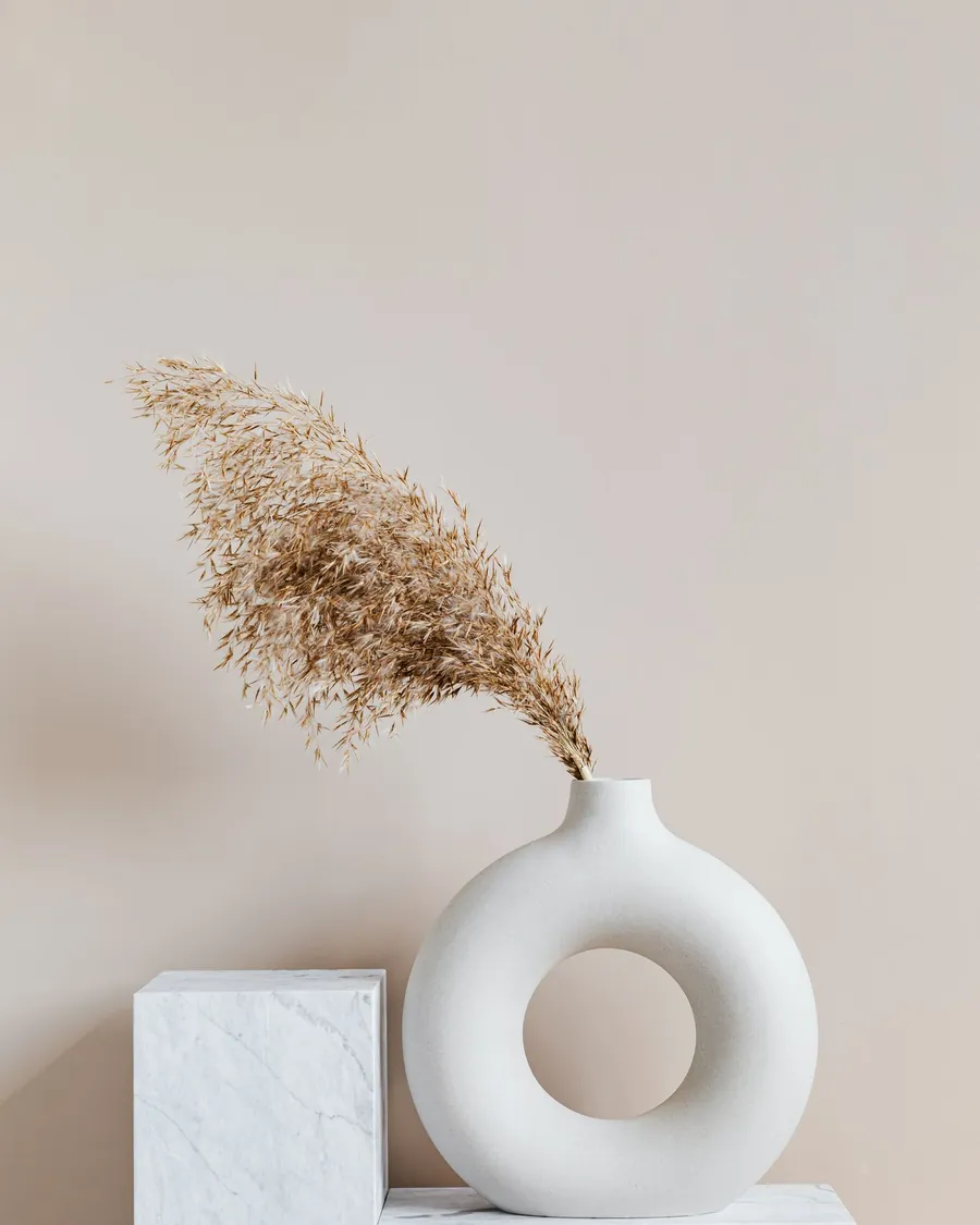 Ring-shaped white ceramic vase with dried grass on a marble plinth